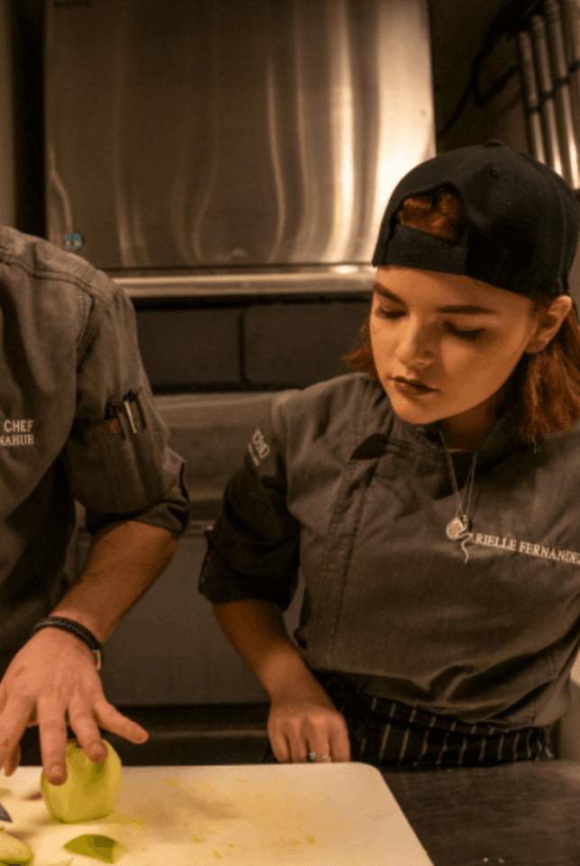 Woman sous chef wearing hat, watching someone chop apples off-camera