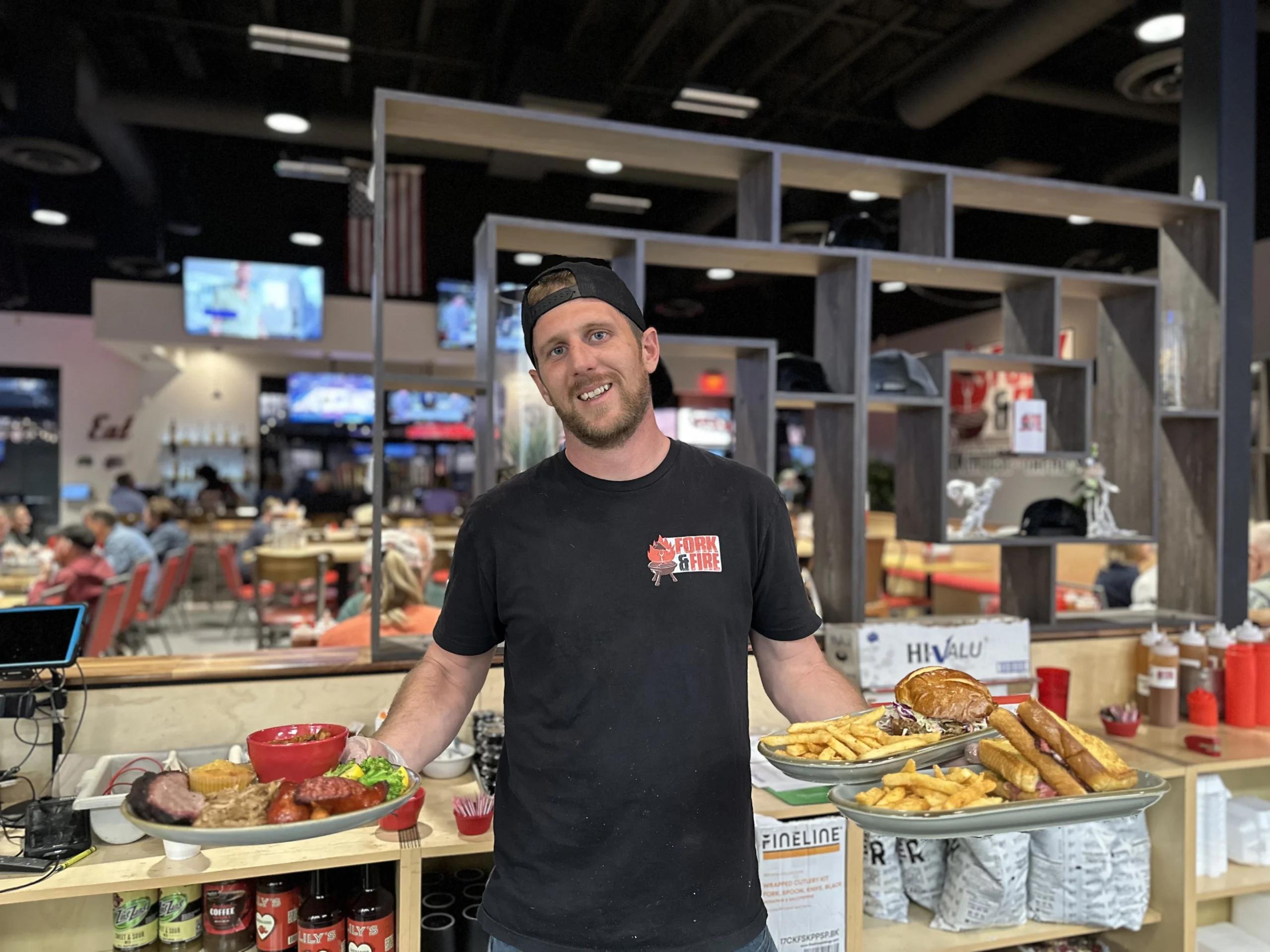 Employee at Fork & Fire holding three dishes.